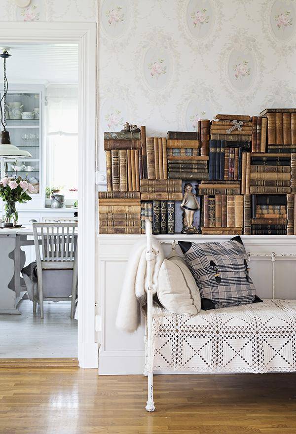 Vintage couch with white metal frame and lacy throw in front of stacked, antiquarian books on sideboard; view into dining room t