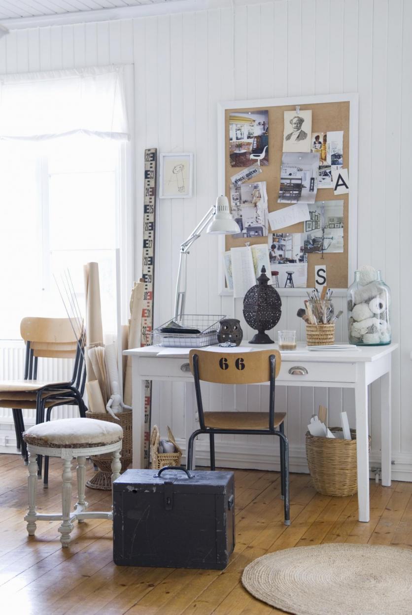 Vintage stool and trunk in front of desk against white-painted wooden wall with pinboard